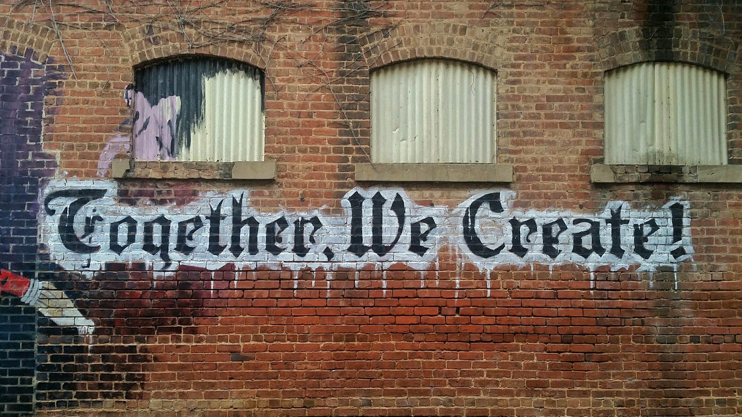 White and black letter "Together We Create" in graffiti style on a brick wall